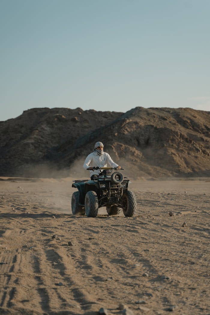 A person riding an ATV across a sandy desert with rocky hills in the background under the daylight.